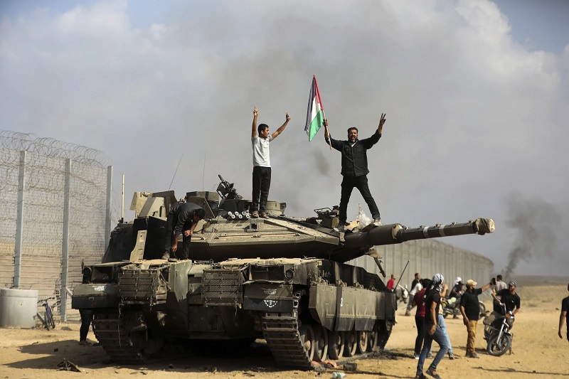 Warga Palestina mengibarkan bendera nasionalnya dan merayakannya dengan tank Israel yang hancur di pagar Jalur Gaza di timur Khan Younis selatan Sabtu, 7 Oktober 2023. AP Photo/Yousef Masoud