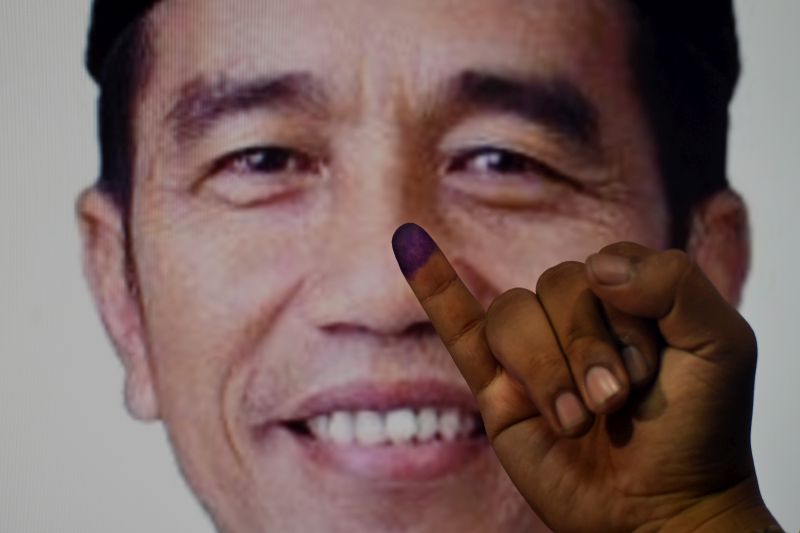 Warga menunjukkan jarinya yang telah dicelupkan tinta usai memberikan hak suaranya dengan latar poster Calon Presiden petahana nomor urut 01 Joko Widodo di Surabaya, Jawa Timur, Rabu (17/4). /Antara Foto.