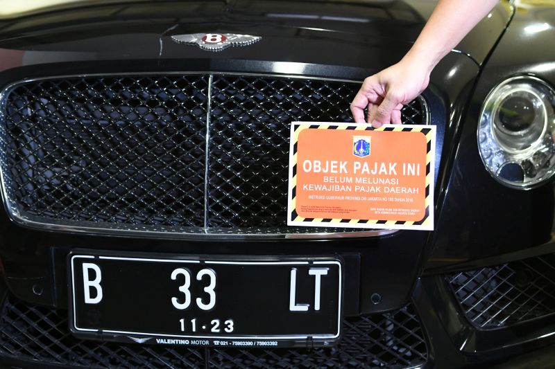 Petugas Samsat Jakarta Utara menunjukkan stiker 'Objek Pajak' di depan mobil mewah Bentley saat razia supervisi pencegahan pajak mobil mewah di Apartemen Regatta, Jakarta Utara di Jakarta, Kamis (5/12/2019). Foto Antara/M Risyal Hidayat.