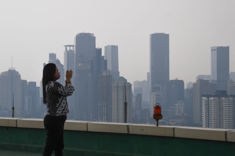 Seorang perempuan memotret gedung bertingkat yang terlihat samar karena kabut polusi di Jakarta, Jumat (5/7). /Antara Foto. 
