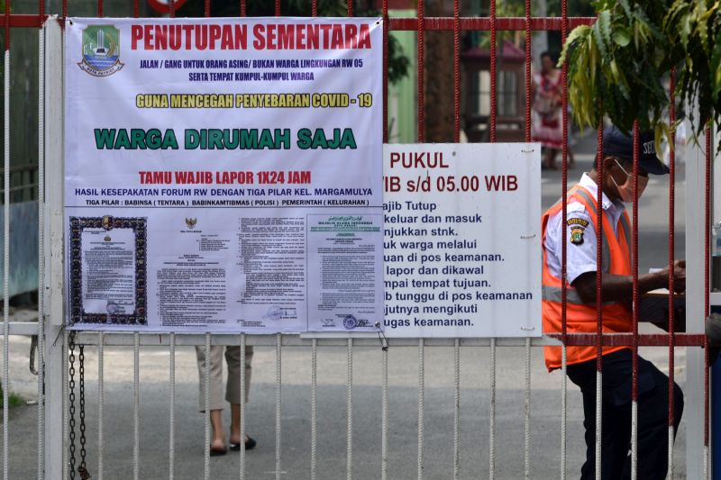 Petugas keamanan menjaga pintu masuk salah satu perumahan yang telah dipasang imbauan agar warga berada di rumah saja di Bekasi, Jawa Barat, Minggu (29/3/2020). Foto Antara/Suwandy.