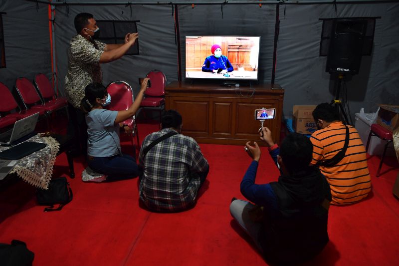  Sejumlah wartawan meliput melalui monitor televisi, keterangan pers Gubernur Jawa TImur Khofifah Indar Parawansa tentang perkembangan Virus Corona, di tenda wartawan, di halaman Gedung Negara Grahadi, Surabaya, Jawa Timur, Jumat (27/3/2020). Foto Antara/Zabur Karuru.