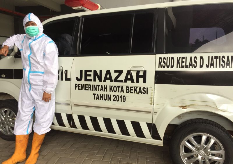 Seorang anggota tim TGC Kota Bekasi berpose di depan mobil ambulans sebelum berangkat menuju tempat evakuasi jenazah Covid-19. Setiap personel yang turun evakuasi mesti dilengkapi alat perlindungan diri. Alinea.id/Rohman Wibowo