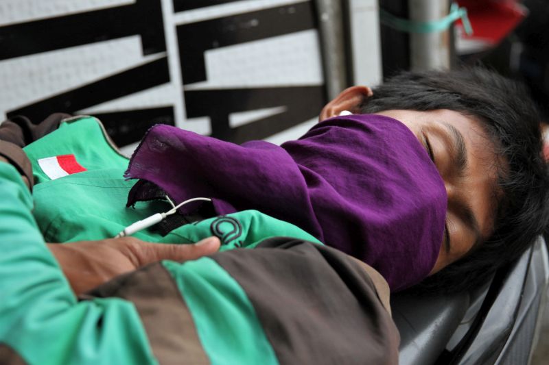 Pengemudi ojek daring tertidur diatas sepeda motornya tak jauh dari salah satu rumah makan akibat sepinya orderan di Kendari, Sulawesi Tenggara, Rabu (8/4). /Foto Antara
