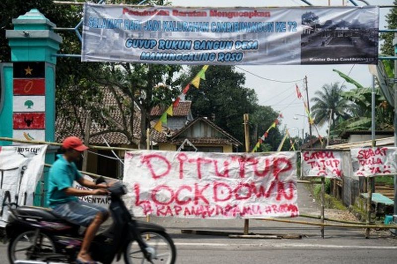 Warga melintas di dekat akses masuk kampung yang ditutup di kawasan Pakem, Sleman, D.I Yogyakarta, Jumat (27/3). /Foto Antara