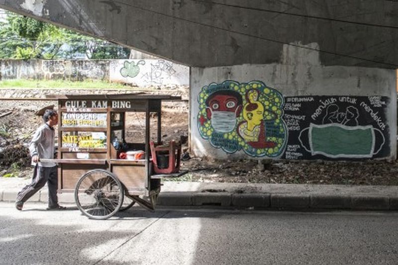 Pedagang kaki lima berjalan di dekat mural bertema pencegahaan penyebaran virus Corona atau COVID-19 di Jakarta, Rabu (1/4). /Foto Antara