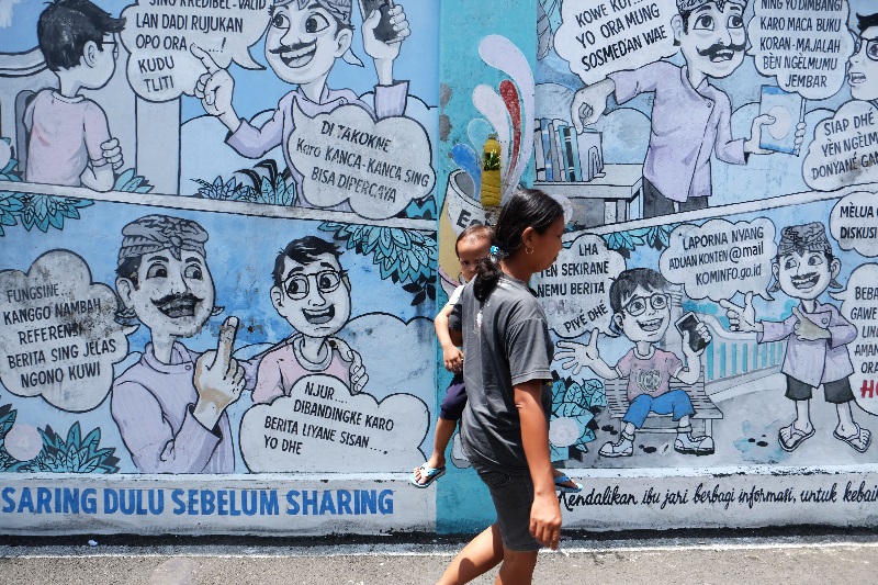 Warga melewati mural (lukisan dinding) komik antihoaks di Kampung Hepi, Joho, Manahan, Solo, Jawa Tengah, Selasa (7/4).Foto Antara/Maulana Surya/foc.