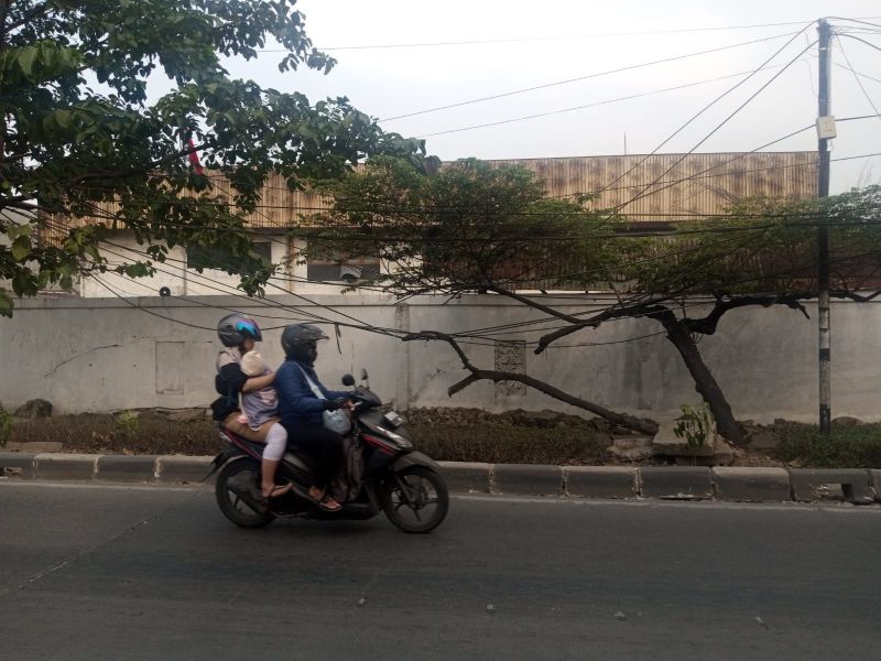 Seorang pengendara sepeda motor dan keluarganya melintasi kabel yang menjuntai di Jalan Haji Kincan, Rawa Buaya, Cengkerang, Jakarta Barat, Minggu (6/8/2023). Alinea.id/Kudus Purnomo Wahidin