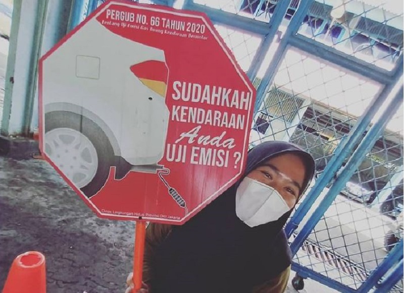 Seorang perempuan mengangkat poster berisi ajakan kepada warga untuk menguji emisi kendaraan sesuai aturan. /Foto Instagram @uji_emisi_jakarta