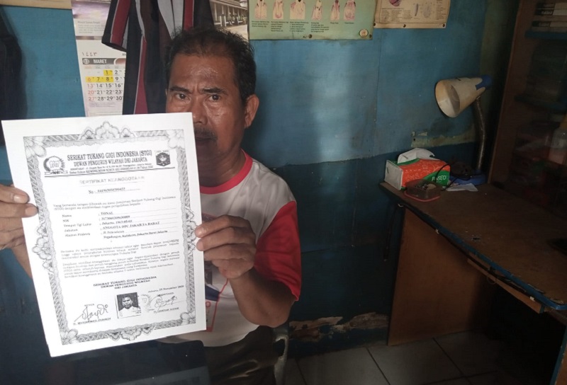 Tonal, 56 tahun, menunjukkan sertifikat resmi tukang gigi miliknya di kiosnya di Kalideres, Jakarta Barat, Senin (28/3). Alinea.id/Kudus Purnomo Wahidin