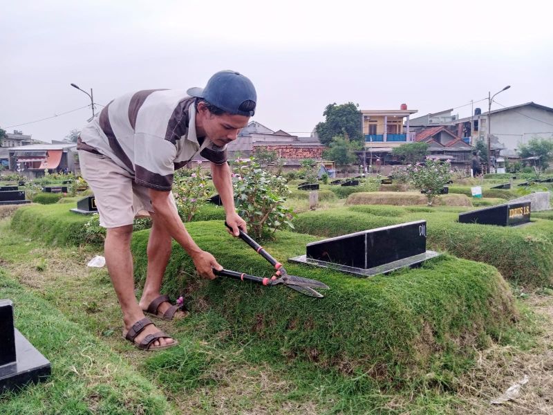Petugas perawat makam, Deden, tengah memotong rumput di tempat permakaman umum (TPU) Tegal Alur, Kalideres, Jakarta Barat, Kamis (21/4/2022). Alinea.id/Kudus Purnomo Wahidin.