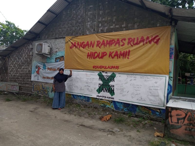 Seorang warga Pulau Pari, Kepulauan Seribu, DKI Jakarta, Asmania tengah berdiri di depan spanduk bernada protes terhadap ancaman kerusakan lingkungan akibat krisis iklim, Kamis (9/2/2023). Alinea.id/Kudus Purnomo Wahidin
