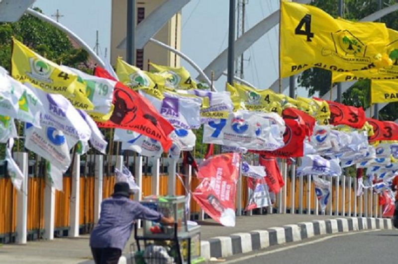 Pedagang mendorong gerobak berisi buah melintas di depan sejumlah bendera partai politik nasional yang dipasang di jembatan Pantee Pirak, Kota Banda Aceh, Sabtu (23/3/2019)./Foto Antara/Ampelsa