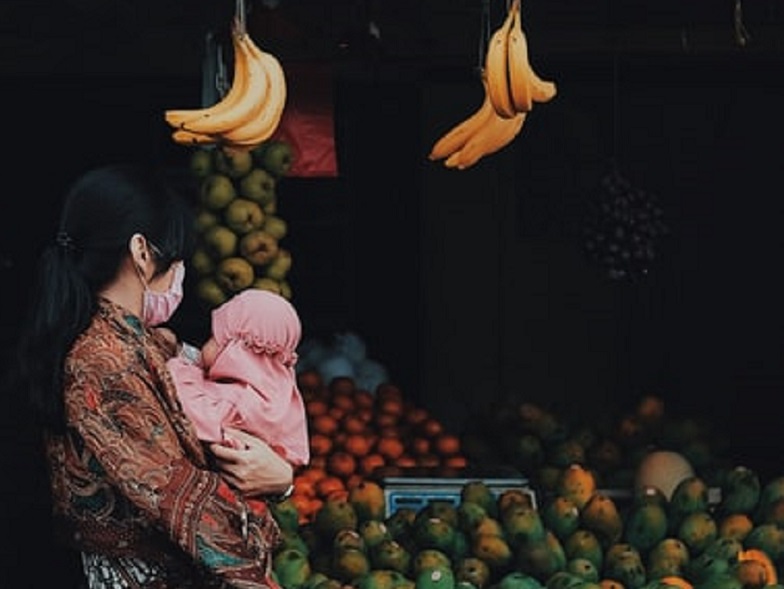 Ilustrasi perempuan belanja di pasar tradisional sambil menggendong anaknya. /Foto Unsplash/ Arif Riyanto